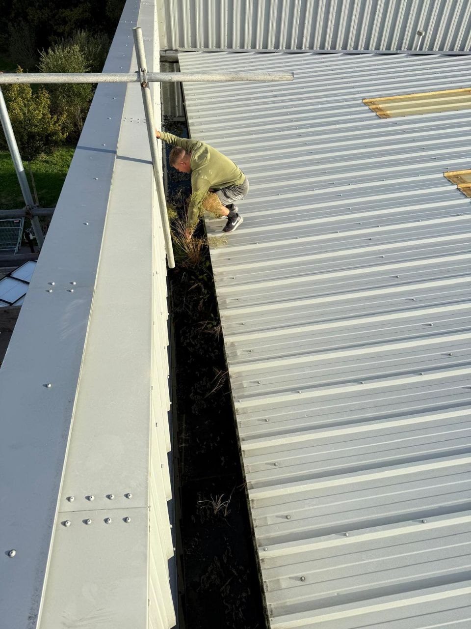 Operative in PPE cleaning an industrial metal roof at height in West Sussex