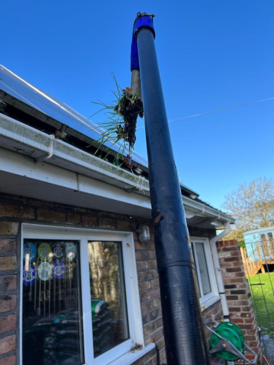 Lifting moss and grass clear of a gutter with a reach-pole gutter vacuum in West Sussex